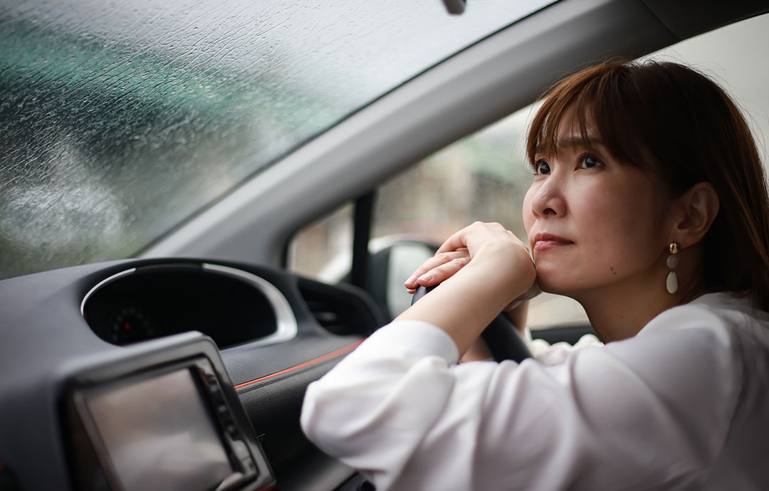 車内から雨の外を眺める女性